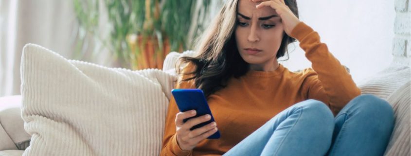 Woman sitting on a lounge looking at her phone contemplating "do I need a mortgage broker"